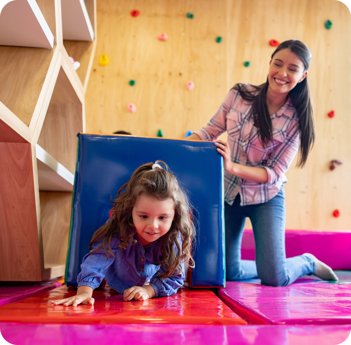 Child crawling through play tunnel, smiling adult